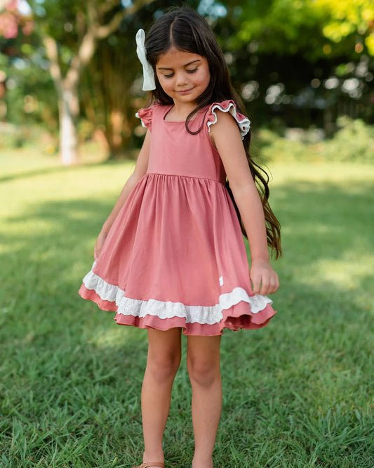 Young girl in a pink dress standing on grass with trees in the background